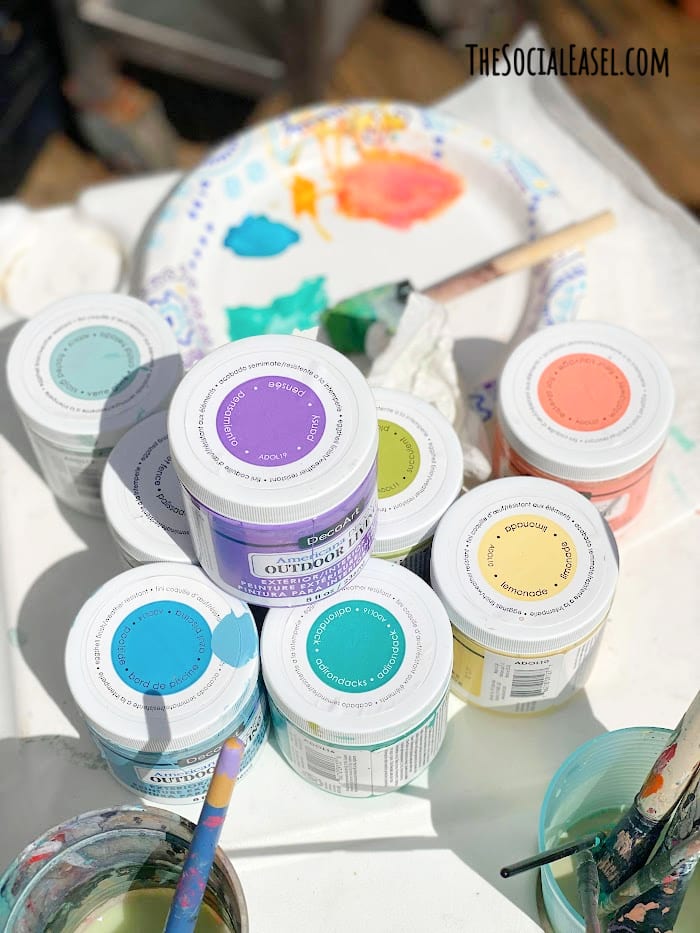 DecoArt Outdoor Craft Paint stacked on a  table with painting supplies