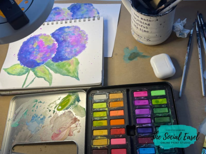 Painting workspace with paints and pad of paperHow to Paint Watercolor Hydrangeas_The Social Easel