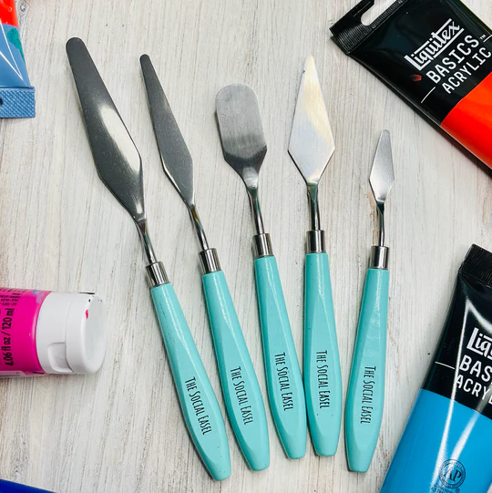 The Social Easel Palette Knives with teal handles on a table with paint