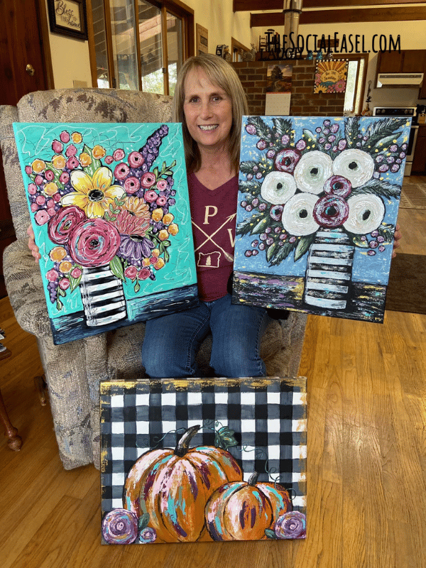 Laurie holding 3 paintings 