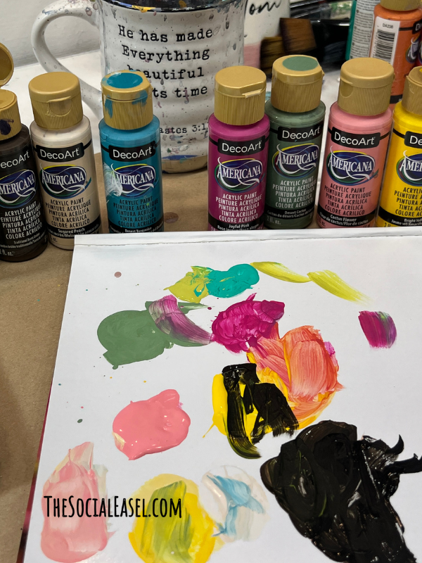 pink, yellow, black, green paint on a pallet. Some of the colors are mixed together to create more shades. 