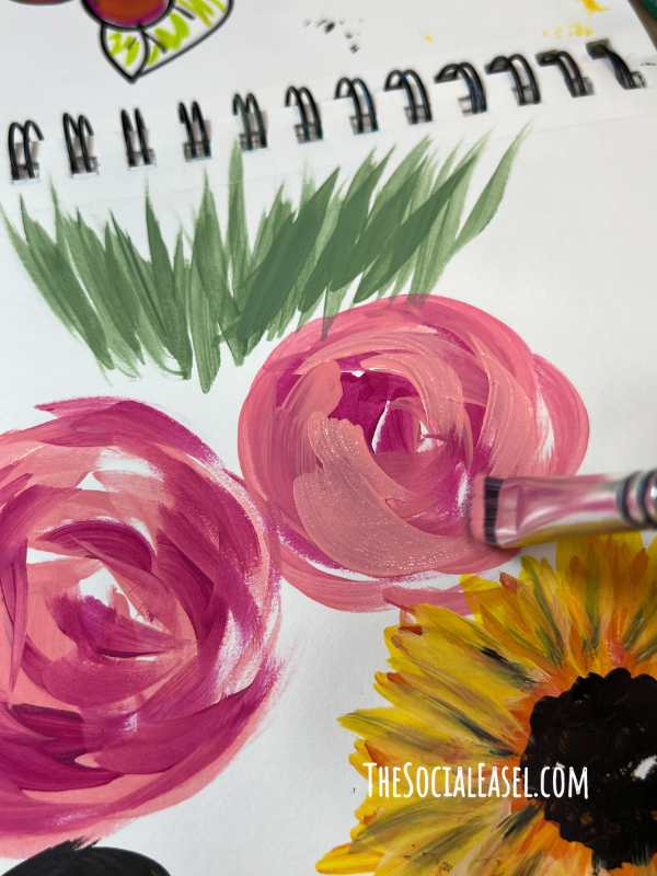 Christie painting with a large angle paintbrush to making 2 abstract pink flowers. 