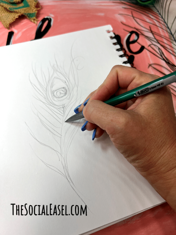 Christie sketching a peacock feather on a mixed media pad. 