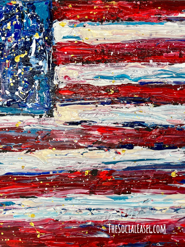 A palette knife painting loose interpretation of an American Flag. On the left side a blue square with lots of spatter, dots, and brush strokes in mostly blue with accents of gold black, white. Red and white textured stipes with spatters of gold and some paint strokes of a lighter blue to accent the flag stripes. 