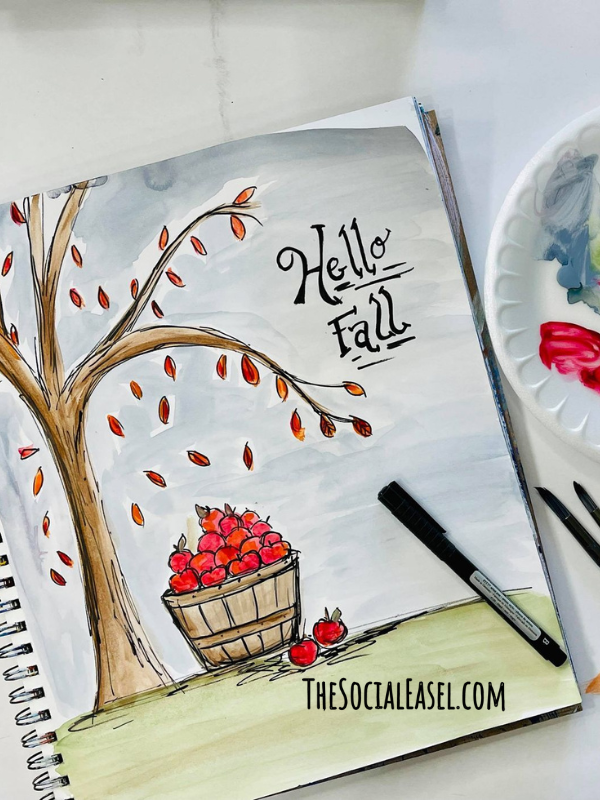 Multi Media Pad with Hello Fall underlined. A black outline marker, a brown tree trunk with falling leaves and a full basket of red apples at the bottom. 