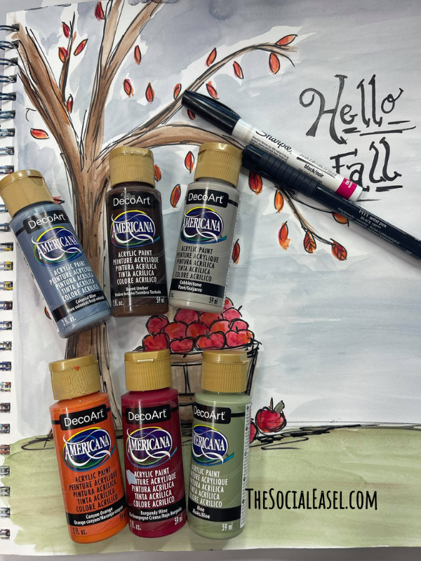 A few supplies used to create the Fall Bushel of Apples painting. Blue, brown, gray, orange, red, and green paint. Displayed on a multi media pad with the Fall Bushel of Apples painting. A sharpie for outlining. 