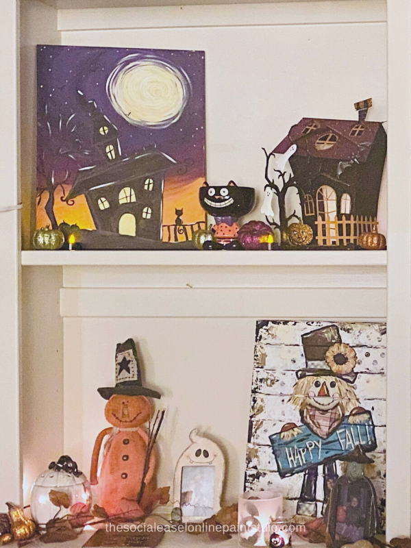 Display of Christie Hawkins canvas art for fall. A haunted house with haunted house decor. And a scarecrow happy fall painted on wood pallet with fall decorations around it. 