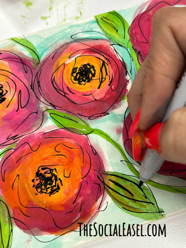 Christie using a black paint pen to add lines to leaves on a floral painting.