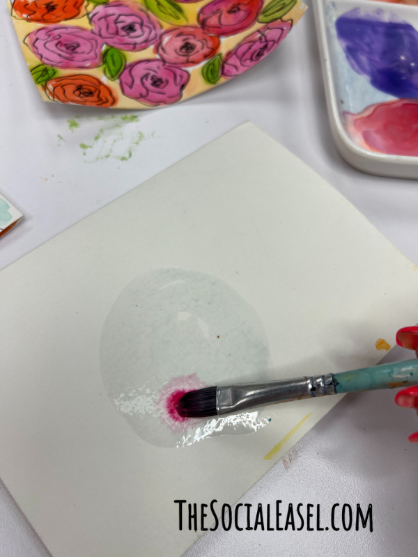Christie demonstrating how to use watercolor paint to make a circle to make a flower.