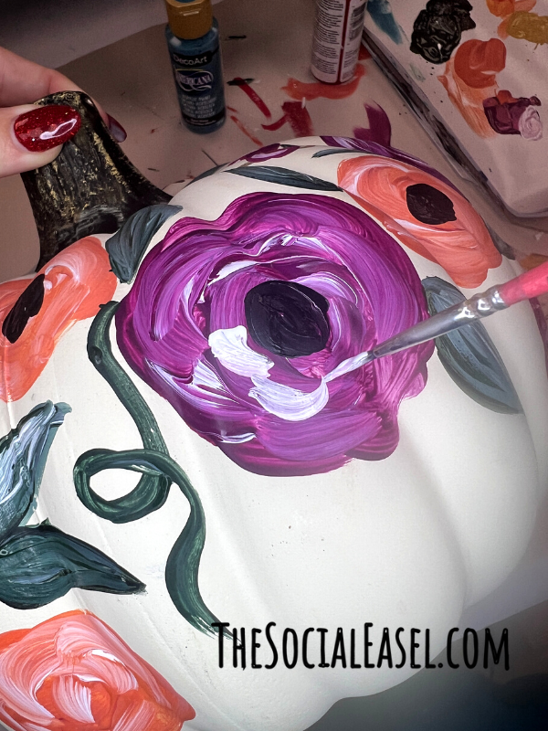 Christie using a small paintbrush and white paint to add layers to a purple flower.