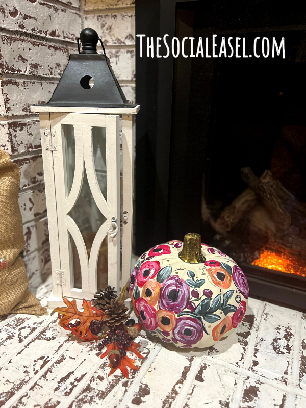 A handpainted white pumpkin with bold blooms displayed with a fall scene.