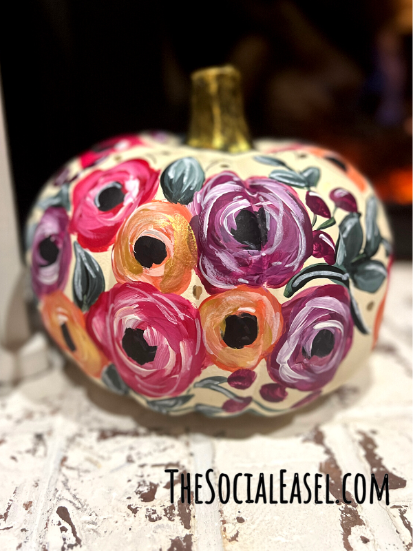  A white painted pumpkin with bold blooms of pink, purple, and orange. Black centers, and green leaves, purple berries. 
