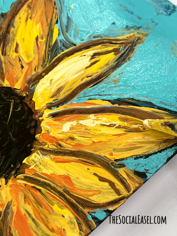 A Pallet knife painting using a teal blue background. A large sunflower with a dark center, gold, yellow, and orange paint used to create each petal. Showing half the flower.