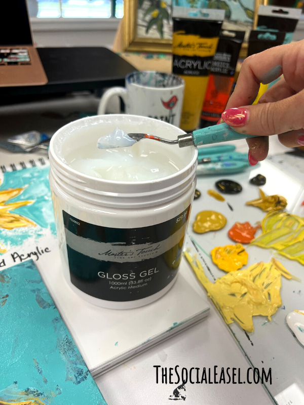 A container of gloss gel and Christie using her pallet knife to take some out.